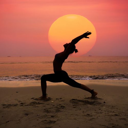 Silhouette young woman practicing yoga on the beach at sunrise